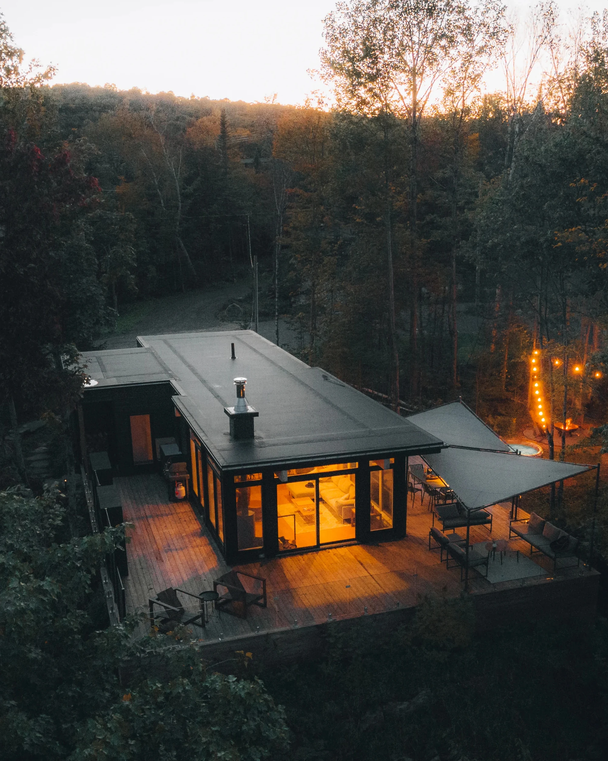 Aerial view of WOLM Cabin glowing warmly in the forest at dusk